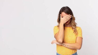 Oldukça zayıf bir kadın stresli, utanmış ya da üzgün görünüyor, baş ağrısı var, yüzünü eliyle kapatıyor.