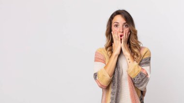 Oldukça zayıf bir kadın şok olmuş ve korkmuş hissediyor, ağzı açık ve elleri yanaklarında korkmuş görünüyor.