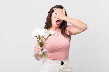 Güzel bir kadın şok olmuş, korkmuş ya da korkmuş görünüyor. Yüzü elle kaplanmış ve elinde dekoratif bir saksı tutuyor.