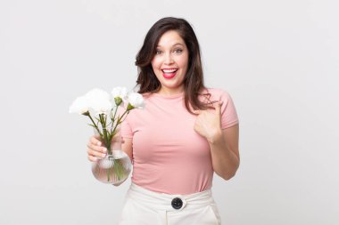 Güzel bir kadın kendini mutlu hissediyor ve heyecanlı ve elinde dekoratif bir saksıyla kendini işaret ediyor.