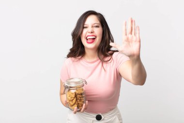 Güzel bir kadın gülümsüyor ve arkadaş canlısı görünüyor. Beş numarayı gösteriyor ve elinde cam bir kurabiye şişesi tutuyor.