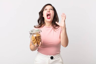 Güzel bir kadın ellerini havaya kaldırıp bağırıyor ve elinde cam bir kurabiye şişesi tutuyor.