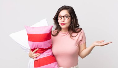 Güzel bir kadın şaşkın ve şaşkın hissediyor pijama giyiyor ve yastık tutuyor.