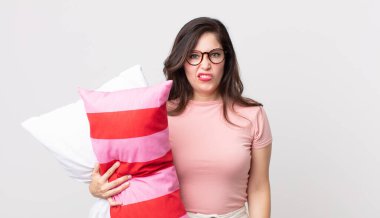 Güzel bir kadın şaşkın ve kafası karışmış görünüyor pijama giyiyor ve yastık tutuyor.