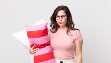 Güzel bir kadın üzgün, üzgün ya da kızgın, pijama giymiş ve elinde yastıkla yan tarafa bakıyor.