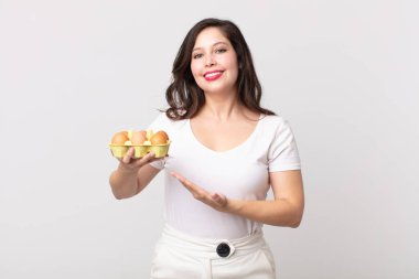 Güzel bir kadın neşeyle gülümsüyor, mutlu hissediyor ve bir konsept gösteriyor ve bir yumurta kutusu tutuyor.