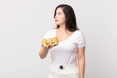 Güzel bir kadın profil görünümünde düşünüyor, hayal ediyor ya da hayal ediyor ve elinde bir yumurta kutusu tutuyor.