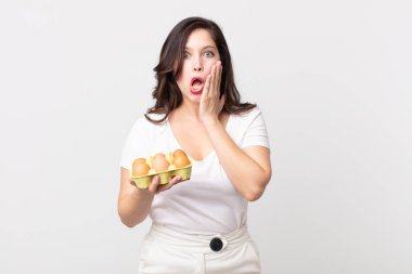 Güzel bir kadın şok olmuş, korkmuş ve elinde bir yumurta kutusu tutuyor.