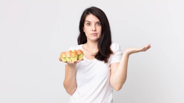 Güzel bir kadın şaşkın, şaşkın, şüpheci ve elinde bir yumurta kutusu tutuyor.