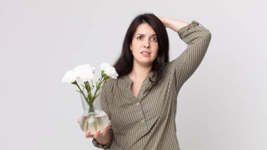 Güzel bir kadın stresli, endişeli ya da korkmuş, elleri başının üstünde ve elinde dekoratif bir çiçek tutuyor. Kulaklıklı bir yardımcı ajan.