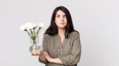 Güzel bir kadın omuz silkiyor, kafası karışık ve kararsız hissediyor ve elinde dekoratif bir çiçek tutuyor. Kulaklıklı bir yardımcı ajan.