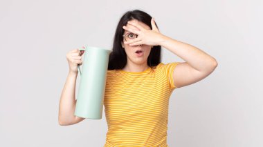 Güzel bir kadın şok olmuş, korkmuş ya da korkmuş görünüyor. Yüzü elle kaplanmış ve elinde kahve termosu tutuyor.