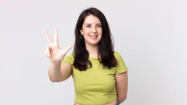 Güzel bir kadın gülümsüyor ve arkadaş canlısı görünüyor. Üç ya da üç numarayı gösteriyor. Elleri önde, geri sayıyor.