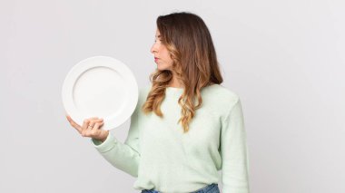 Profil görünümlü oldukça zayıf bir kadın hayal ediyor ya da hayal ediyor boş bir tabak tutuyor ve boş bir tabak tutuyor.