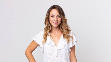 Oldukça zayıf bir kadın mutlu bir şekilde gülümsüyor, eli kalçasında ve kendinden emin, olumlu, gururlu ve arkadaş canlısı bir tavırla.