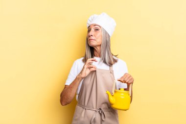 Orta yaşlı şef kadın kibirli, başarılı, pozitif ve gururlu görünüyor, kendini gösteriyor ve elinde bir çaydanlık tutuyor.