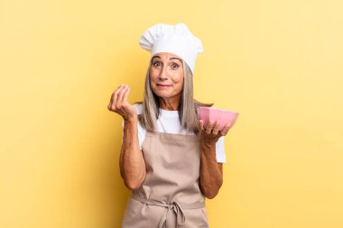 Orta yaşlı aşçı kadın kapiş ya da para hareketi yapıyor, sana borçlarını ödemeni söylüyor! Ve boş bir tencere tutuyor.