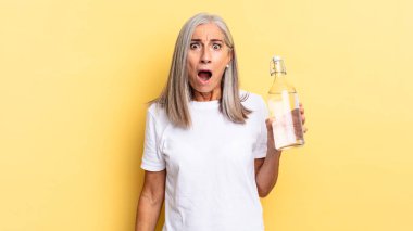 Şok olmuş ya da şaşırmış görünüyor, ağzı açık bakıyor, vay canına diyor ve elinde bir su şişesi tutuyor.