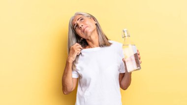 Stresli, endişeli, yorgun ve hayal kırıklığına uğramış, gömleğini çekmiş, sıkıntılı görünüyor ve elinde bir su şişesi tutuyor.