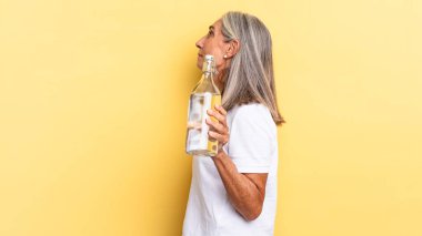 Profil görünümünde uzayı kopyalamak, düşünmek, hayal etmek veya hayal etmek ve bir su şişesi tutmak.