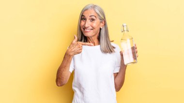 Heyecanlı ve şaşırmış görünüyor. Yanları ve yukarıları göstererek boşluğu kopyalıyor ve elinde bir su şişesi tutuyor.