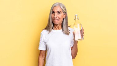 Şaşırmış ve kafası karışmış görünüyor, gergin bir hareketle dudağını ısırıyor, sorunun cevabını bilmiyor ve elinde bir su şişesi tutuyor.