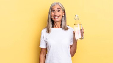 Mutlu ve hoş bir şekilde şaşırmış, büyülenmiş ve şok olmuş bir ifadeyle heyecanlanmış ve elinde bir su şişesi tutuyordu.