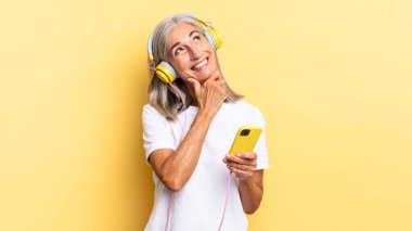 Mutlu, kendinden emin bir ifadeyle gülümsüyor, elleri çenesinde, merak ediyor ve kulaklıkla yan tarafa bakıyor.