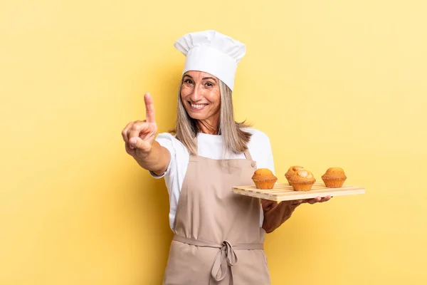 Küchenfrau Mittleren Alters Lächelt Und Schaut Freundlich Zeigt Nummer Eins — Stockfoto