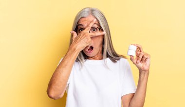 Şok olmuş, korkmuş ya da dehşete düşmüş bir halde, yüzünüzü ellerinizle kapayıp parmaklarınızın arasına bakıp, ilaç şişesini tutuyorsunuz.