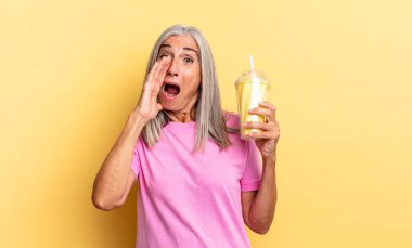 Mutlu, heyecanlı ve pozitif hissediyorum. Elleri ağızda, bağırıyor ve milkshake tutuyor.