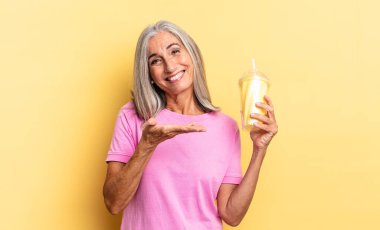 Neşeli bir şekilde gülümsüyor, mutlu hissediyor ve bir konsepti fotokopi alanında, avuç içinde bir milkshake tutarak gösteriyor.