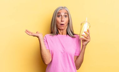 Şaşırmış ve şok olmuş görünüyor, çenesi düşmüş bir nesneyi elinde açık bir elle tutuyor ve bir milkshake tutuyor.