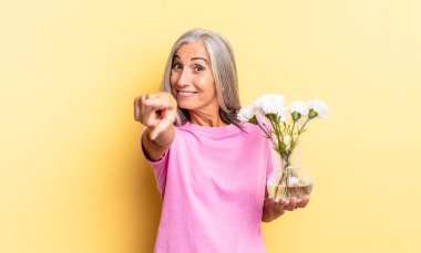 Tatmin olmuş, kendine güvenen, dost canlısı bir gülümsemeyle kameraya çevrilmiş, elinde süslü çiçeklerle seni seçmiş.