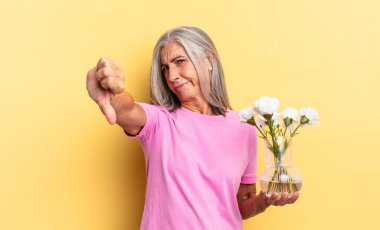 Kızgın, kızgın, sinirli, hayal kırıklığına uğramış ya da hayal kırıklığına uğramış. Elinde dekoratif çiçekler olan ciddi bir bakışla baş parmaklarını göstermiyor.