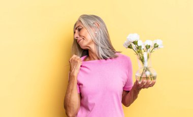 Stresli, endişeli, yorgun ve hayal kırıklığına uğramış, tişörtünü çekmiş, dekoratif çiçekleri tutmakta zorlanmış görünüyor.