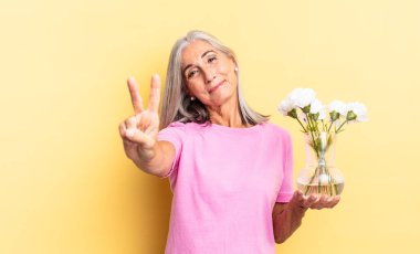 Gülümsüyor ve dost canlısı görünüyor, iki ya da iki numarayı gösteriyor, elinde süslü çiçeklerle geriye doğru sayıyor.