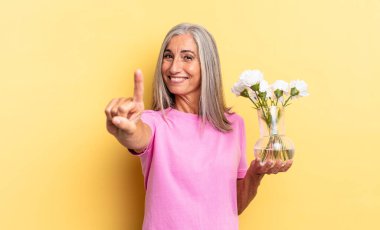 Gülümsüyor ve dost canlısı görünüyor, bir numara ya da ilk eli önde, elinde süslü çiçeklerle geriye doğru sayıyor.