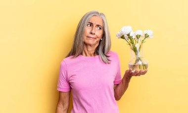 Üzgün, üzgün ya da kızgın hissediyorum ve olumsuz bir tavır takınıyorum, anlaşmazlık içinde çatık kaşlı, elinde dekoratif çiçeklerle.