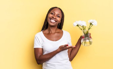 Neşeli bir şekilde gülümseyen, mutlu hisseden ve fotokopi uzayında avucunun içinde bir konsept gösteren. Dekoratif çiçek konsepti