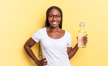 Mutlu bir şekilde gülümsüyor, eli kalçasında ve kendinden emin, olumlu, gururlu ve arkadaş canlısı bir tavırla. su şişesi kavramı