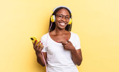 Neşeli bir şekilde gülümseyen, mutlu hisseden, kenarı ve yukarıyı gösteren, kopyalama alanında nesne gösteren ve müzik dinleyen