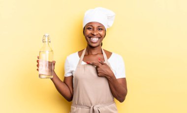Siyah afro şef kadın heyecanlı ve şaşırmış görünüyor. Elinde su şişesi olan bir fotokopi odasını işaret ediyor.