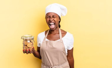 Siyah afro şef kadın agresif bir şekilde bağırıyor, çok kızgın, hayal kırıklığına uğramış, öfkeli ya da sinirli görünüyor, hayır diye bağırıyor. kurabiye konsepti