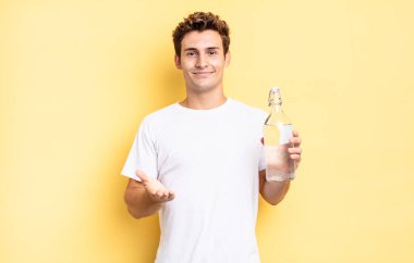 Mutlu bir şekilde gülümseyen, kendine güvenen, olumlu bakışlı, bir nesne ya da konsept sunan ve gösteren. su şişesi kavramı