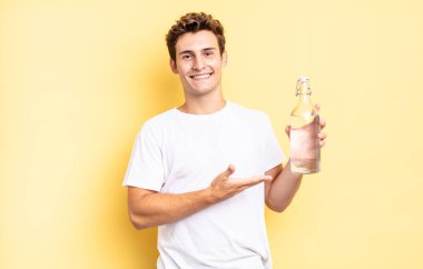 Neşeli bir şekilde gülümseyen, mutlu hisseden ve fotokopi uzayında avucunun içinde bir konsept gösteren. su şişesi kavramı