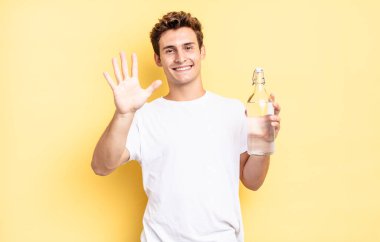 Gülümsüyor ve dost canlısı görünüyor. 5 ya da 5 numarayı gösteriyor. Elleri önde, geriye doğru sayıyor. su şişesi kavramı