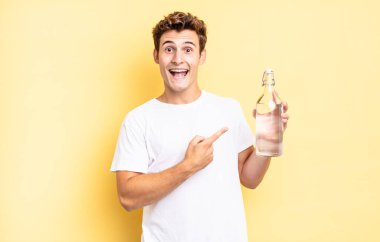 Heyecanlı ve şaşırmış görünüyor. Yana doğru ve yukarı doğru uzayı gösteriyor. su şişesi kavramı