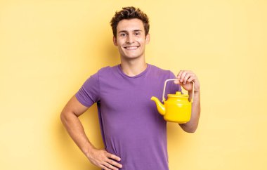 Mutlu bir şekilde gülümsüyor, eli kalçasında ve kendinden emin, olumlu, gururlu ve arkadaş canlısı bir tavırla. çaydanlık konsepti