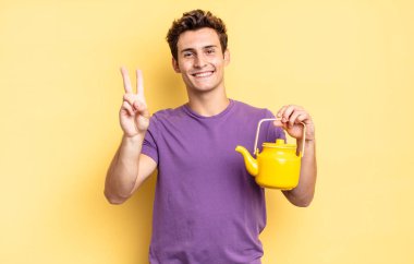 Gülümsüyor ve dost canlısı görünüyor. İki ya da iki numarayı gösteriyor. Elini ileri uzatıp geri sayıyor. çaydanlık konsepti